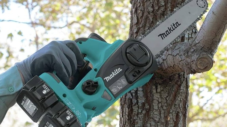 A chainsaw being used to cut a tree branch.