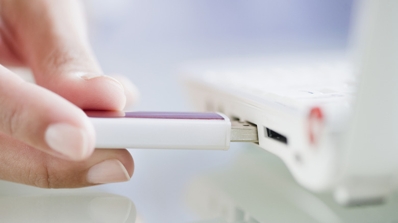 A person plugging a thumb drive into a laptop