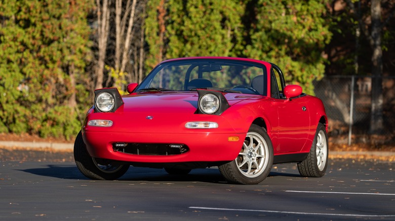 Red 1990s Mazda Miata parked in lot with trees in background