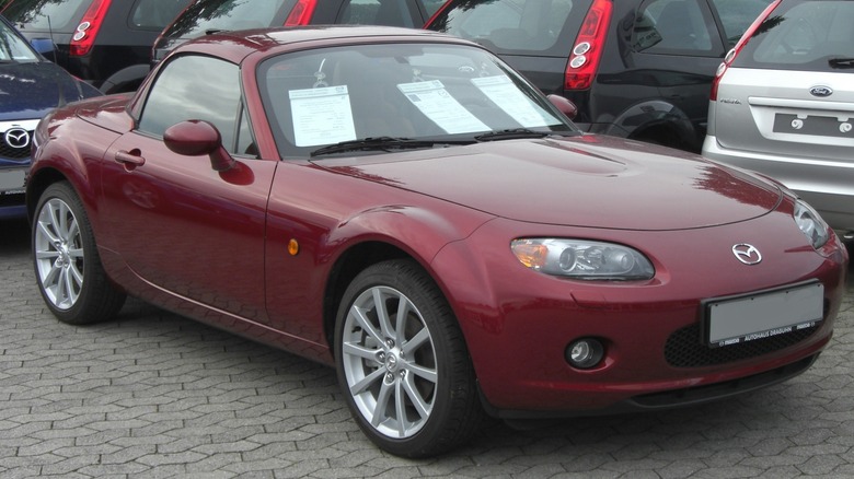 Maroon Mazda Miata parked in dealership lot with window stickers visible