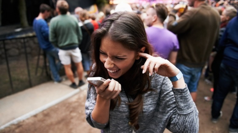 Woman struggling to talk on a phone in a noisy concert environment