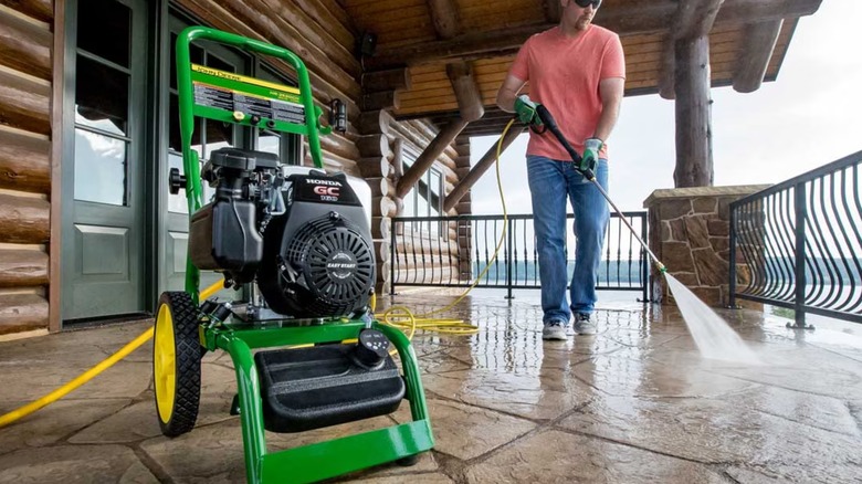 A man washes a patio overlooking the water with a John Deere pressure washer