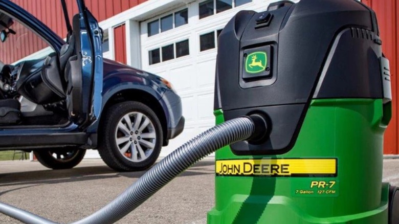 A John Deere wet/dry vacuum in front of a car with an open door