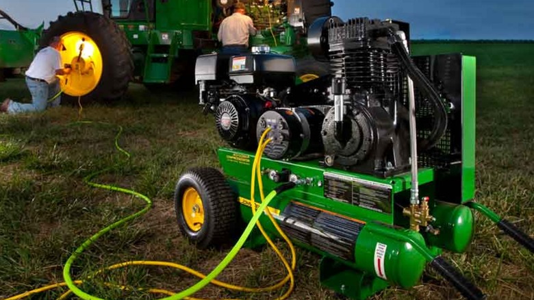 A John Deere Compresserator combo unit attached to a large machine with workers in the background