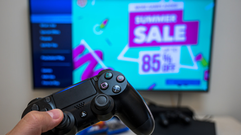 person holding DualShock controller in front of TV with summer sale