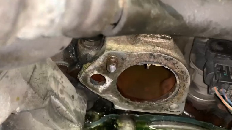 A closeup of a broken bolt on a thermostat housing on a car engine