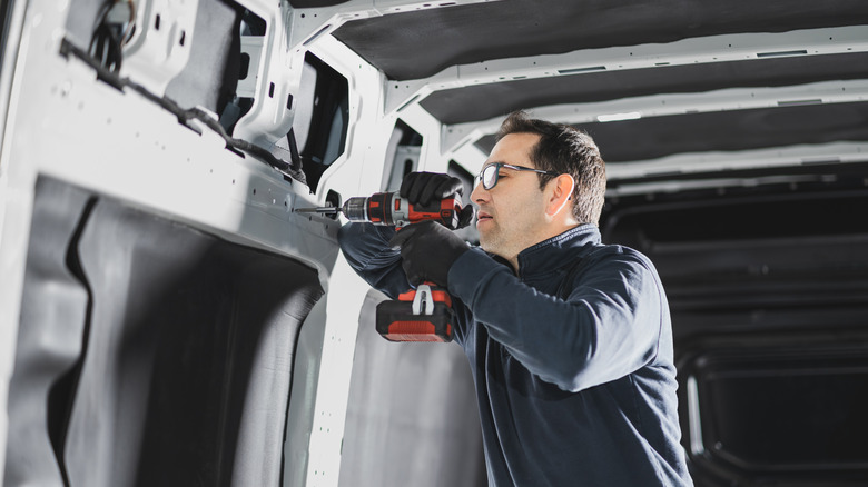 An engineer drilling into a van wall.