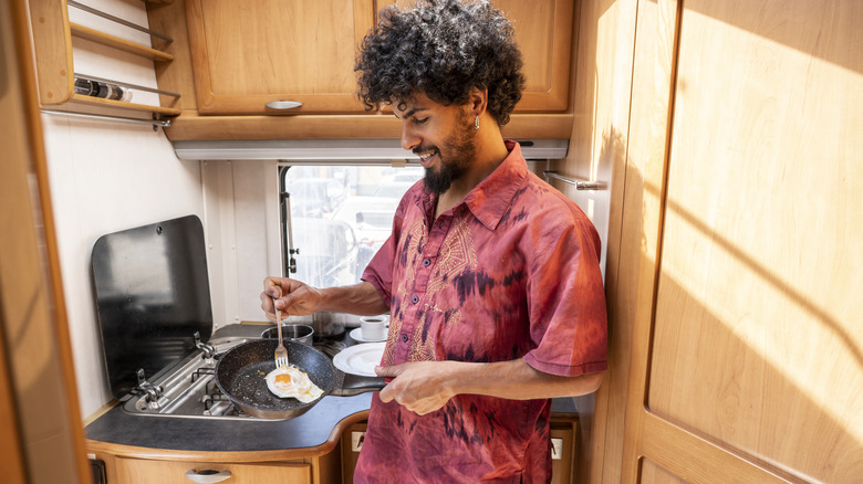 Man frying egg in compact van kitchen with small frying pan