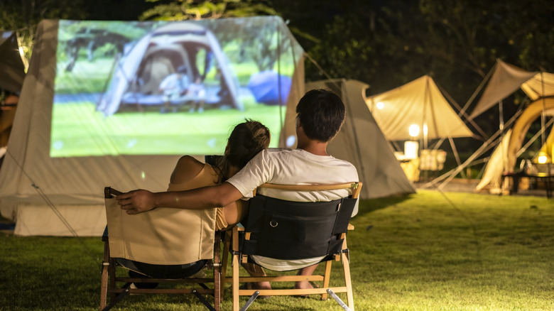 Couple on fold-out chairs watching a projection on the side of a tent