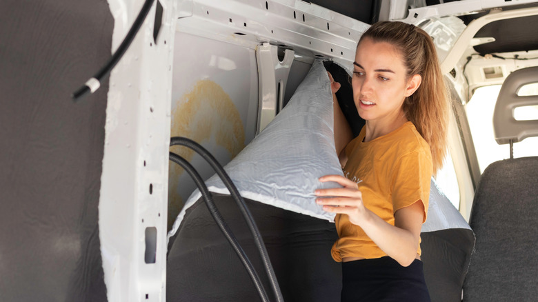 Woman applying adhesive insulation to internal wall of van