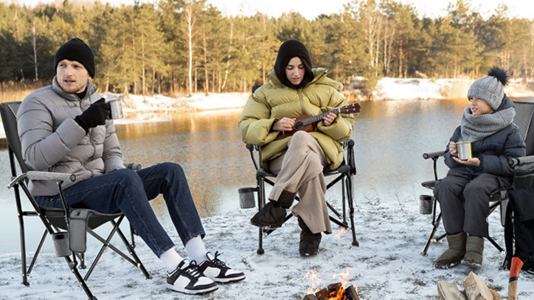 People sitting in camping chairs next to a snowy lake