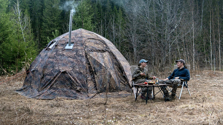 People sitting next to camo tent outside