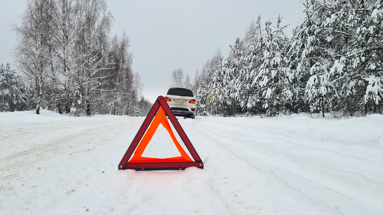 Warning triangle placed in snow behind stranded white SUV