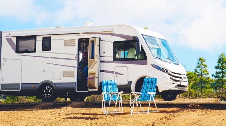 A big RV parked in front of some chairs