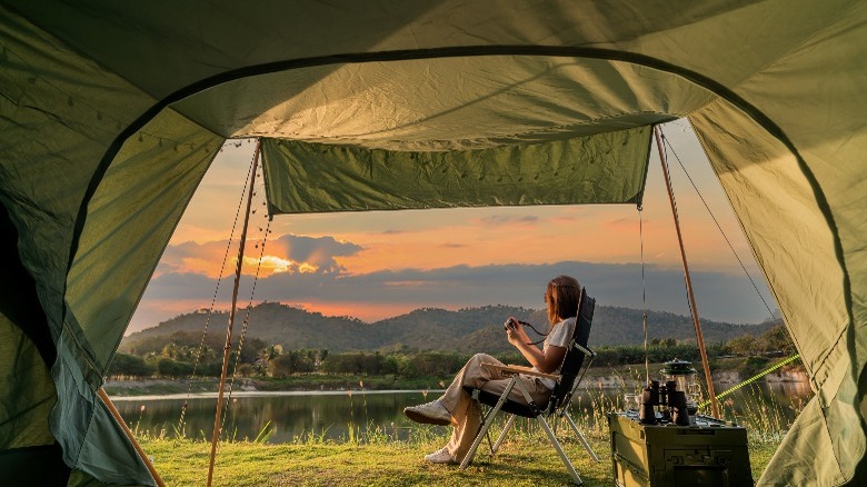 Woman sitting outside tent looking at a lake