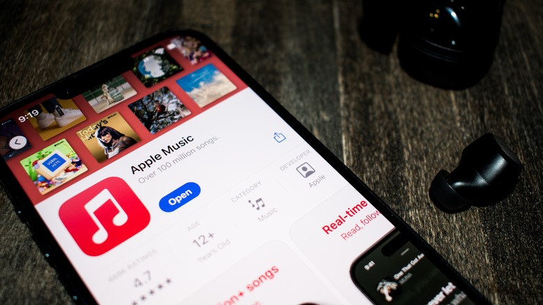 Apple Music app store entry on a phone next to Bluetooth earbuds