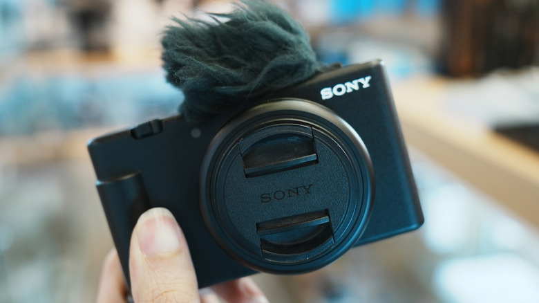 A person holding the Sony ZV-1F camera with the wind screen ataached to the mic