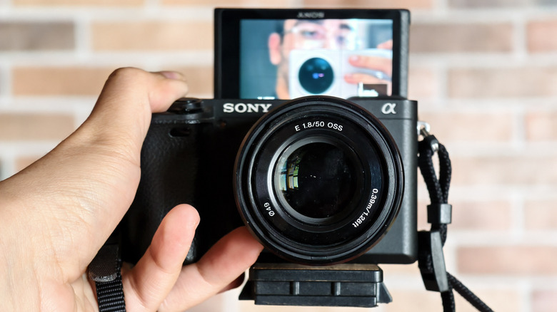 Sony camera with a 50mm lens and a flip screen held in the hand while recording