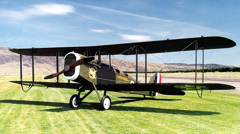 A De Havilland DH-4 on grass near an airstrip.