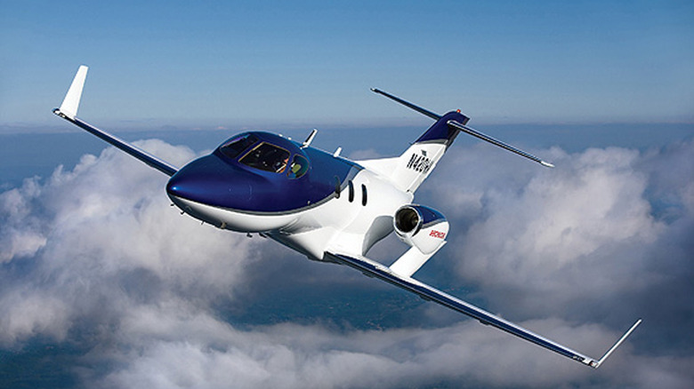 A HondaJet aircraft above fluffy white clouds against a blue sky.