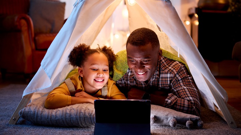 dad and child watching tablet in indoor tent 