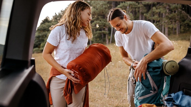 Two people grabbing sleeping bags from their car