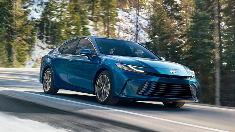 Blue 2025 Toyota Camry on a wooded rural paved road