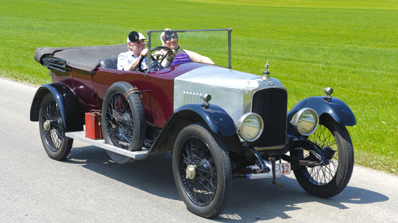 couple driving Vauxhall D-type with field in background