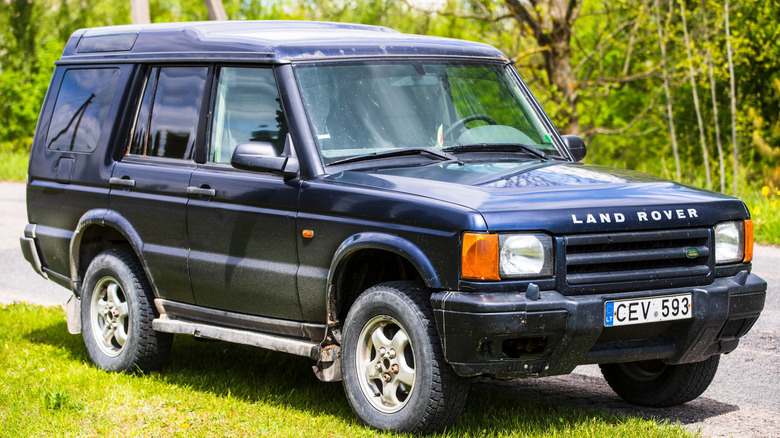 Blue Land Rover Discovery Series II parked on roadside with trees in background