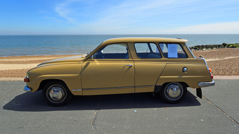 A mustard Saab 95 parked on a road in a coastal area