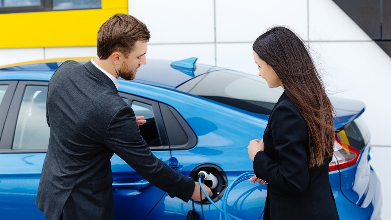 Car salesman showing female client how to charge a car