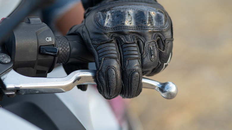 Left hand of a biker with a black leather glove on the clutch lever