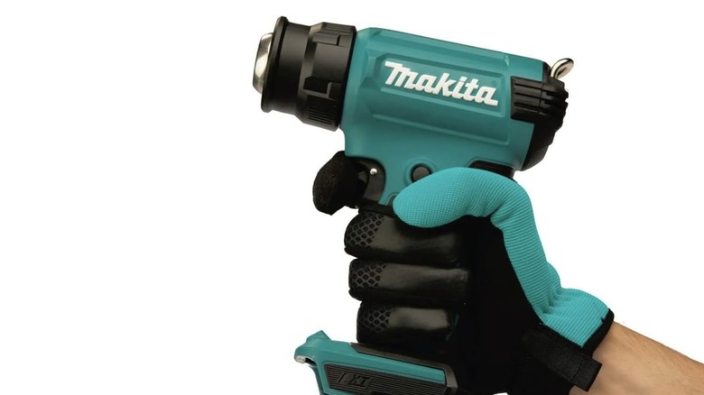 A man holding a Makita heat gun with a white background