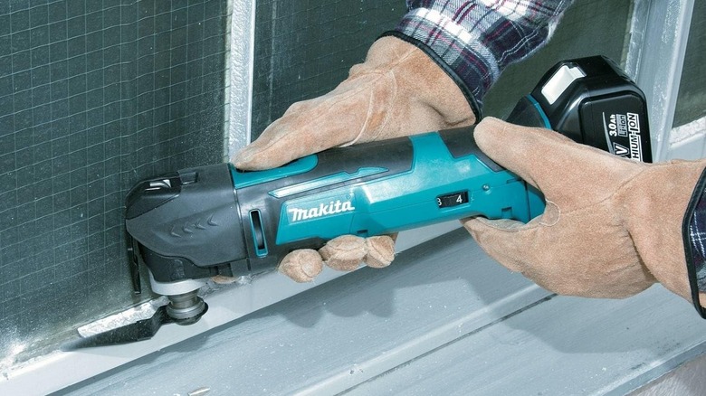 Person using Makita multi-tool on bathroom tiles