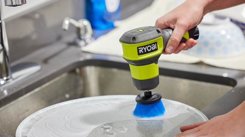 Ryobi scrubber tool being used to clean glass in sink