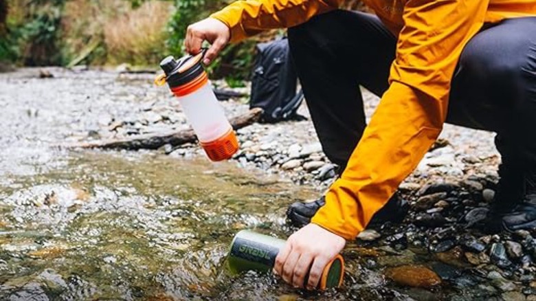 Person using water purifier bottle in creek