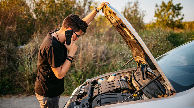 Man looking under his car hood while on the phone