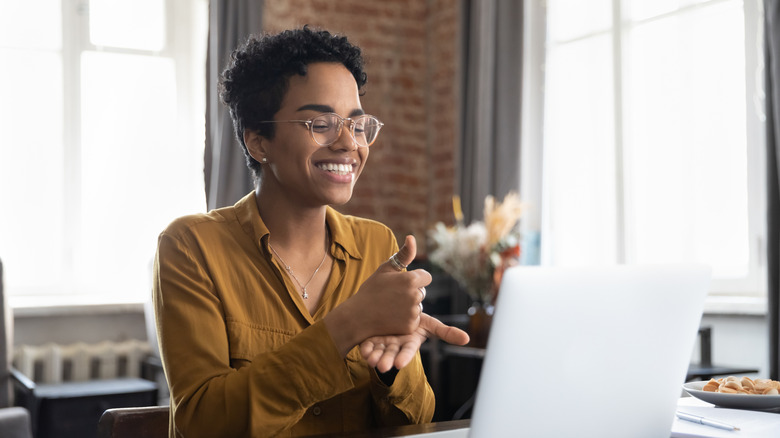 Woman smiling while performing sign language to laptop screen