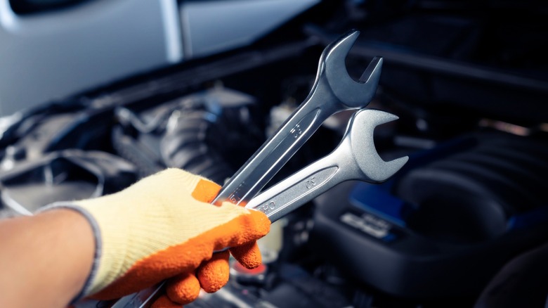 Mechanic holding two wrenches in front of an engine