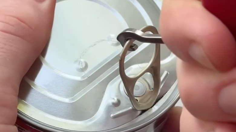 Person pulling a can tab with Swiss Army knife hook