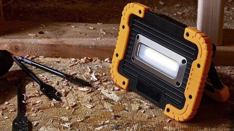 A Braun battery bank work light sitting on a piece of plywood near some drill bits