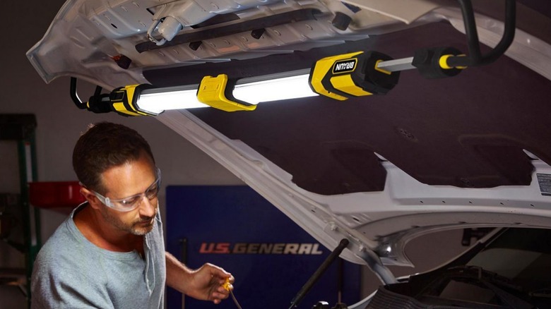 A person working on their car using a Braun underhood light to illuminate the engine bay