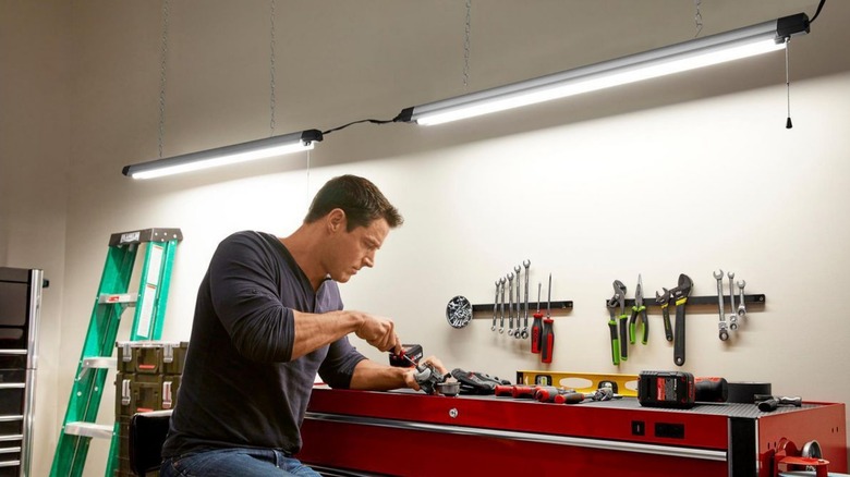 A person working at a work bench with braun hanging shop lights above their head