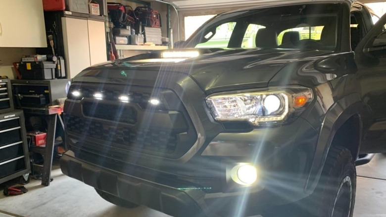 black Toyota Tacoma parked in garage with off-road lights in hood scoop and grille lit up