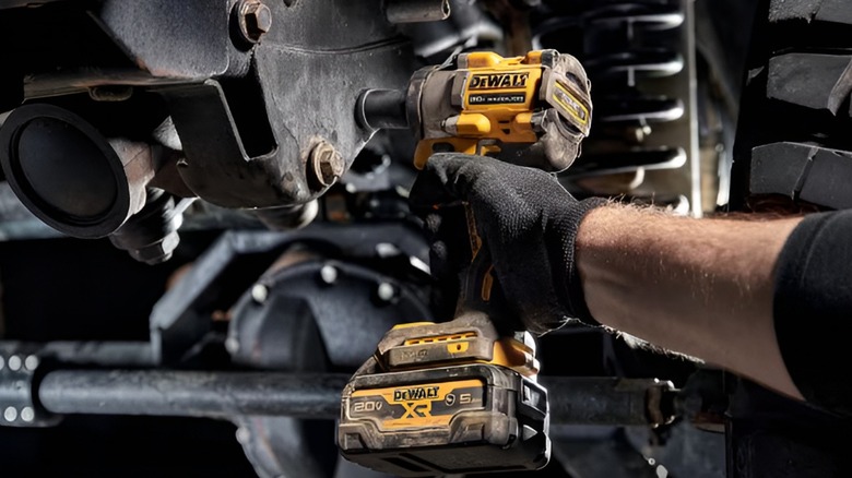 A person using a DeWalt 3/8-inch drive impact wrench on a car's suspension