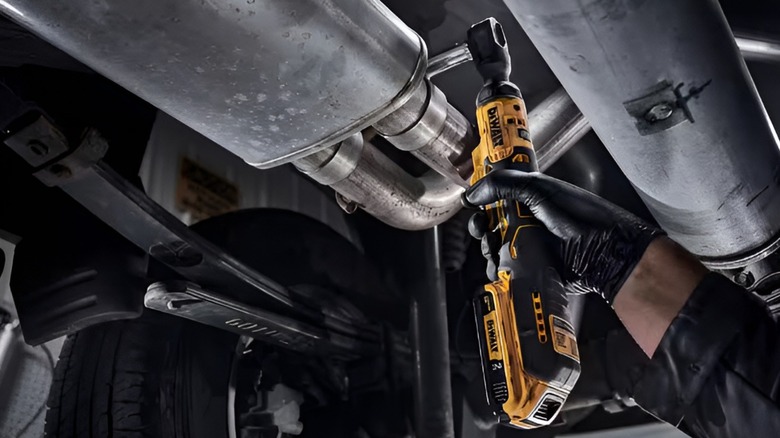 A person using a DeWalt cordless ratchet on a car's exhaust system