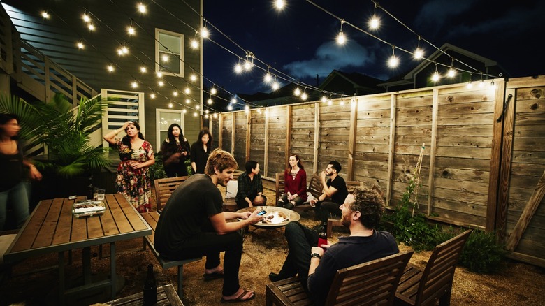 a group of people having an outdoor get together beneath outdoor string lights