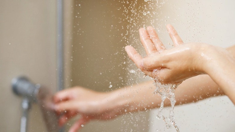 A person turning on their shower and feeling the waterflow with their hand