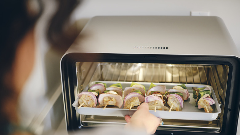 woman putting kebabs in toaster oven