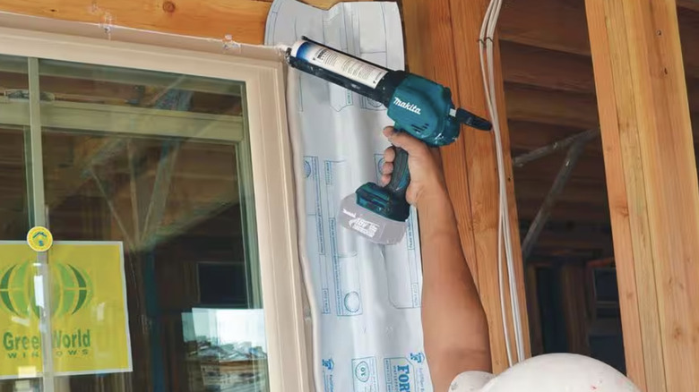 Person using a caulk gun on a window frame